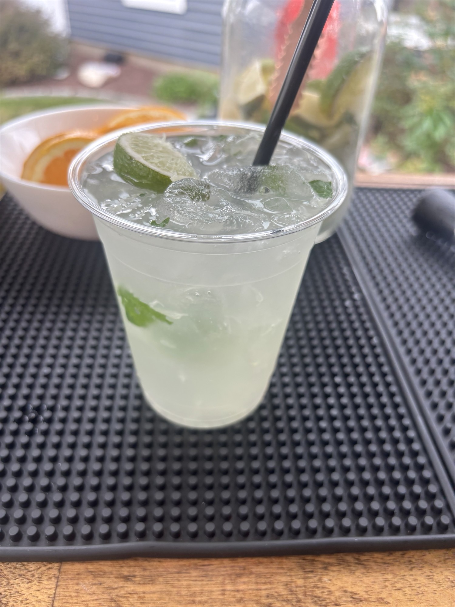 Pale iced drink with a lime slice, green leaves, and a black straw in a clear cup