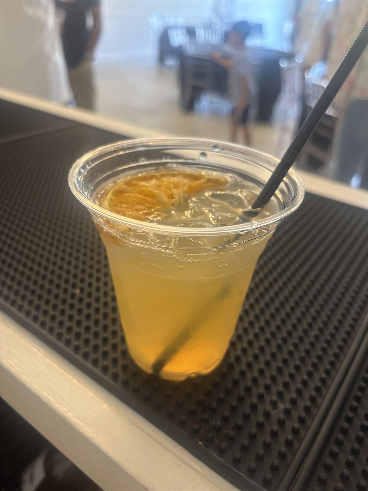 Yellow iced drink in a clear cup with an orange slice and a black straw