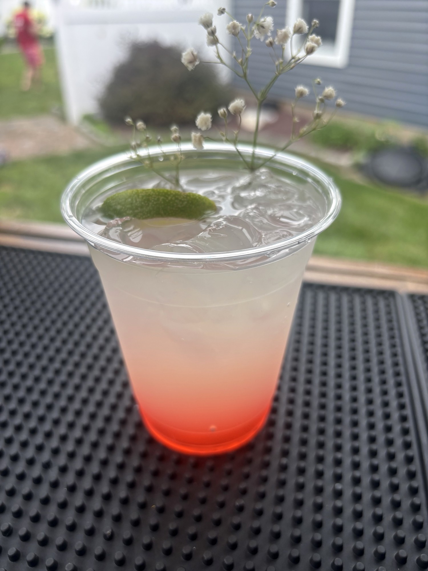 Iced drink with a red layer at the bottom, a lime wedge, and small white flowers in a clear cup