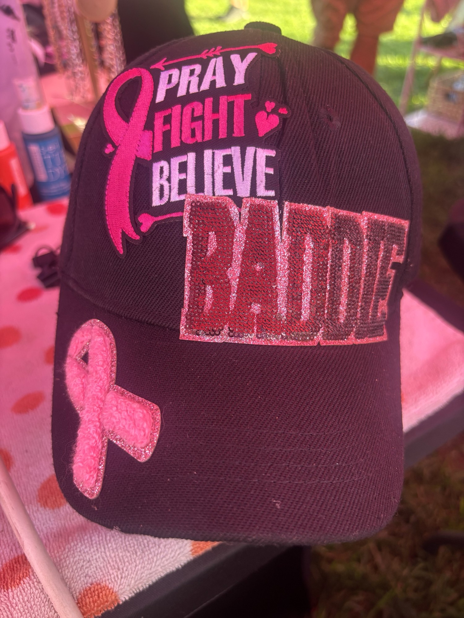 Black cap with pink ribbon patches, Pray Fight Believe lettering, and a sequined Boujee patch
